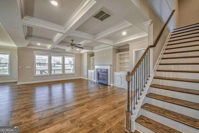 unfurnished living room featuring visible vents, coffered ceiling, a fireplace with flush hearth, wood finished floors, and crown molding