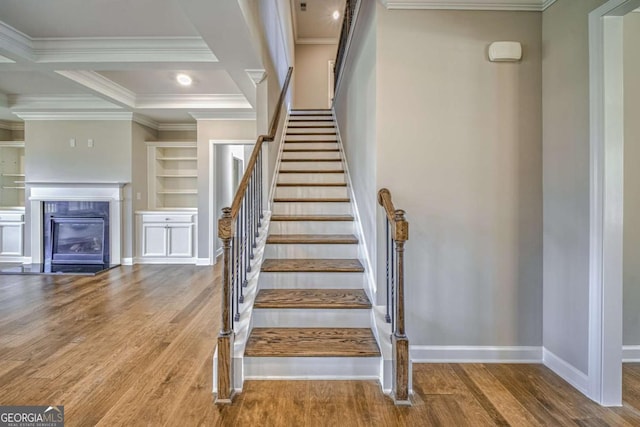 stairs featuring baseboards, coffered ceiling, wood finished floors, crown molding, and built in shelves