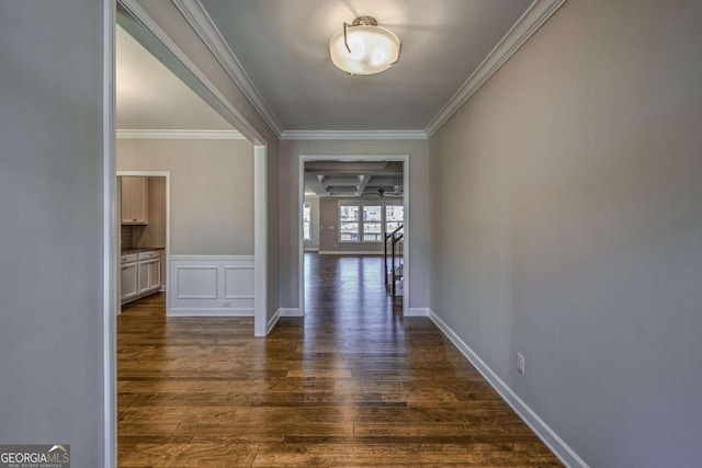 hall featuring baseboards, a decorative wall, dark wood finished floors, and crown molding