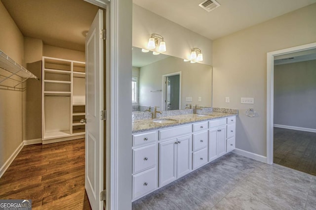 bathroom featuring a sink, wood finished floors, a walk in closet, and visible vents