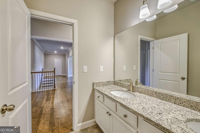 bathroom with wood finished floors, a sink, baseboards, double vanity, and crown molding