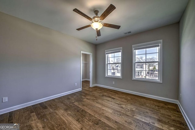 unfurnished bedroom with dark wood finished floors, visible vents, baseboards, a closet, and a walk in closet