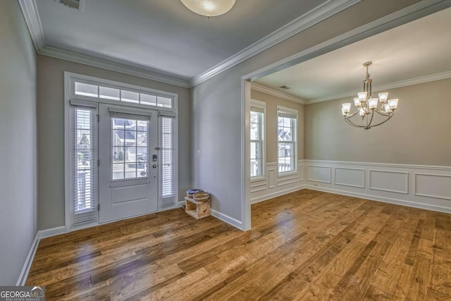 entryway featuring a wainscoted wall, ornamental molding, wood finished floors, a decorative wall, and a notable chandelier