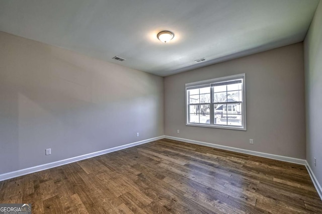 spare room featuring baseboards, visible vents, and dark wood-type flooring