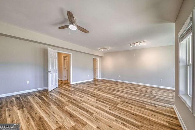 empty room with a ceiling fan, light wood-type flooring, track lighting, and baseboards