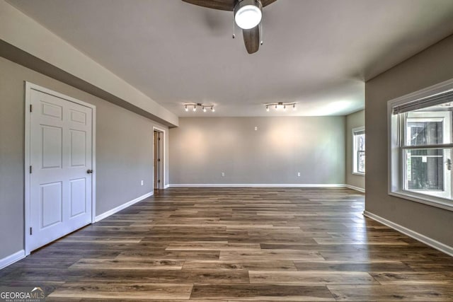 empty room with rail lighting, ceiling fan, baseboards, and dark wood-type flooring