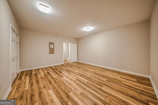 empty room with light wood-type flooring, electric panel, visible vents, and baseboards