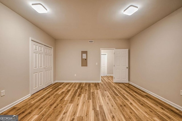 unfurnished bedroom with light wood-style flooring, electric panel, baseboards, and a closet