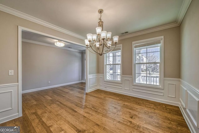 unfurnished dining area featuring visible vents, wainscoting, wood finished floors, an inviting chandelier, and crown molding