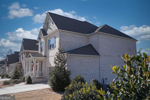 view of property exterior with brick siding, roof with shingles, a garage, cooling unit, and driveway