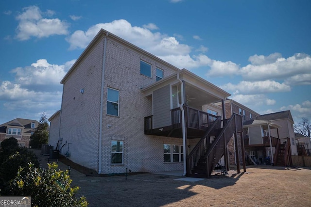 back of house with ceiling fan, stairway, and brick siding