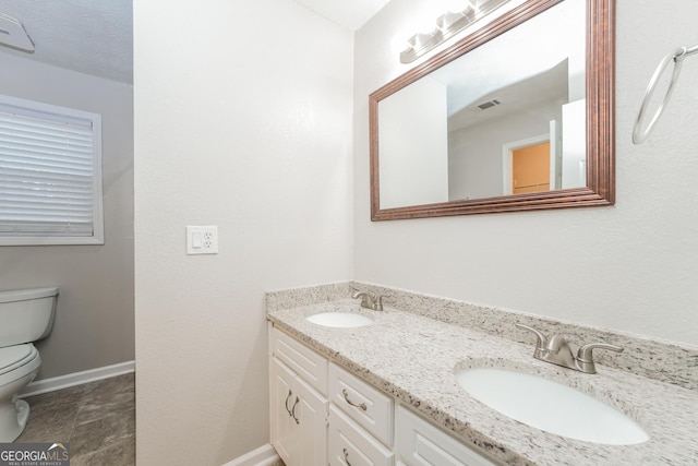 bathroom with visible vents, double vanity, a sink, and toilet