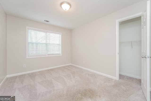 unfurnished bedroom with a closet, light colored carpet, visible vents, and baseboards