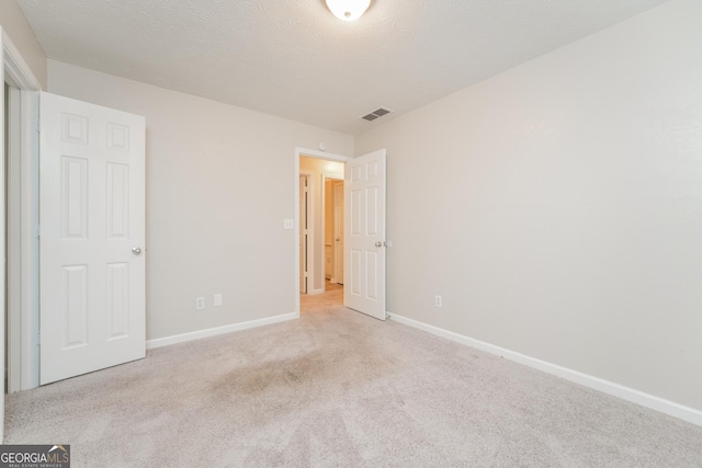 unfurnished bedroom with baseboards, a textured ceiling, visible vents, and light colored carpet