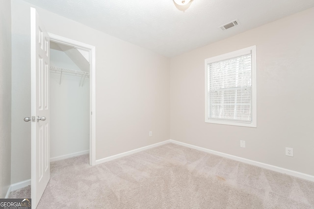 unfurnished bedroom with baseboards, visible vents, light colored carpet, a textured ceiling, and a closet