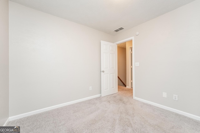 empty room with baseboards, a textured ceiling, visible vents, and light colored carpet