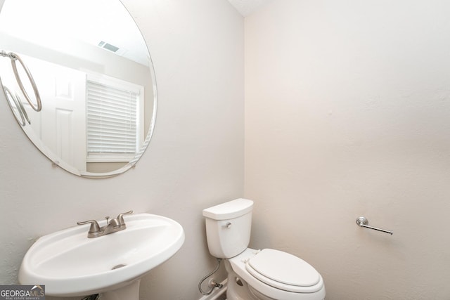 half bathroom featuring toilet, visible vents, and a sink