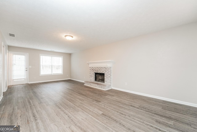 unfurnished living room with a fireplace, wood finished floors, visible vents, and baseboards