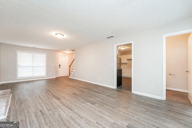 unfurnished living room with a textured ceiling, wood finished floors, visible vents, baseboards, and stairway