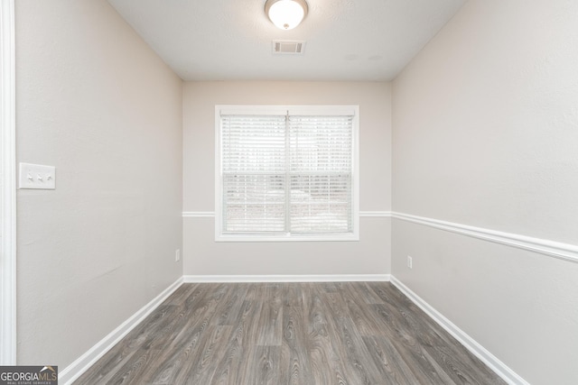 unfurnished room featuring dark wood-style floors, visible vents, and baseboards