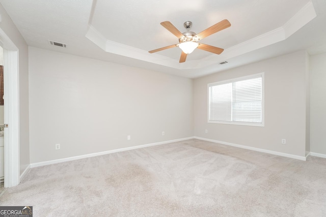 empty room featuring light carpet, a tray ceiling, visible vents, and baseboards