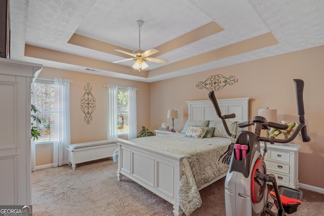 bedroom featuring light carpet, a tray ceiling, and multiple windows