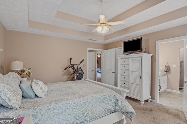 bedroom featuring light carpet, a ceiling fan, visible vents, baseboards, and a tray ceiling