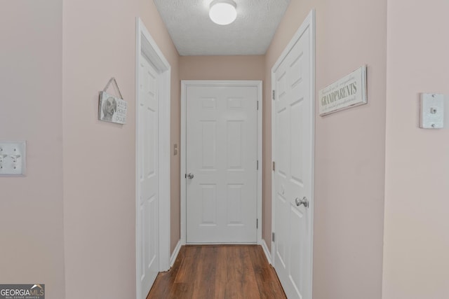 hallway featuring dark wood-style floors, baseboards, and a textured ceiling