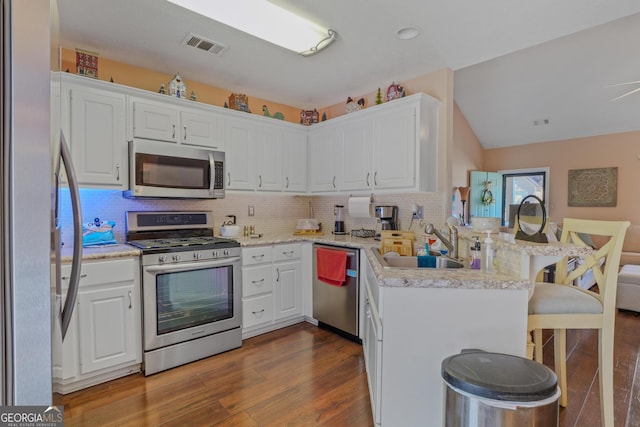 kitchen featuring stainless steel appliances, a peninsula, a sink, white cabinetry, and a kitchen breakfast bar