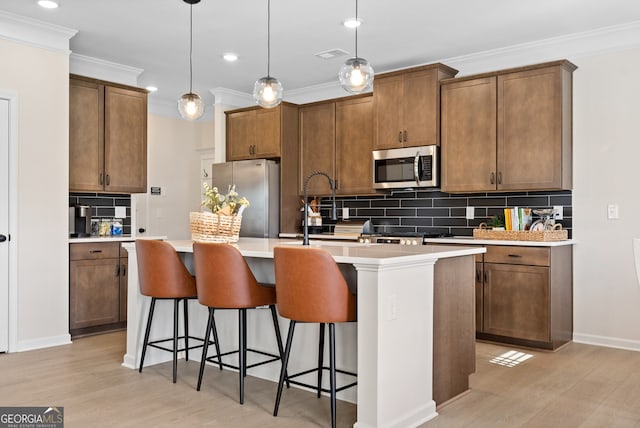 kitchen with appliances with stainless steel finishes, light countertops, brown cabinetry, and a kitchen island with sink