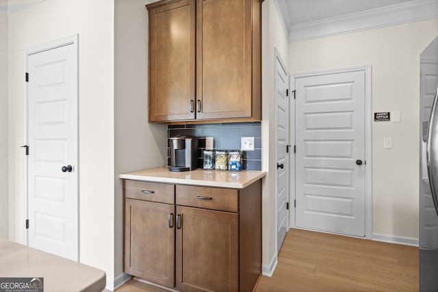 bar with baseboards, light wood finished floors, ornamental molding, freestanding refrigerator, and tasteful backsplash