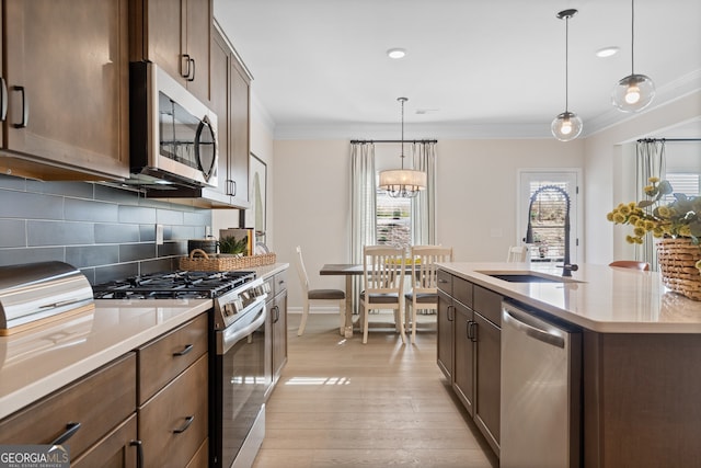 kitchen featuring a center island with sink, stainless steel appliances, light countertops, hanging light fixtures, and a sink