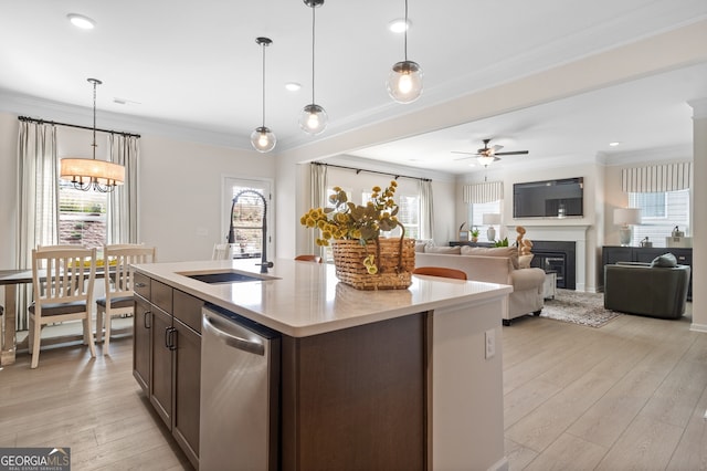 kitchen featuring a kitchen island with sink, light countertops, dishwasher, and decorative light fixtures