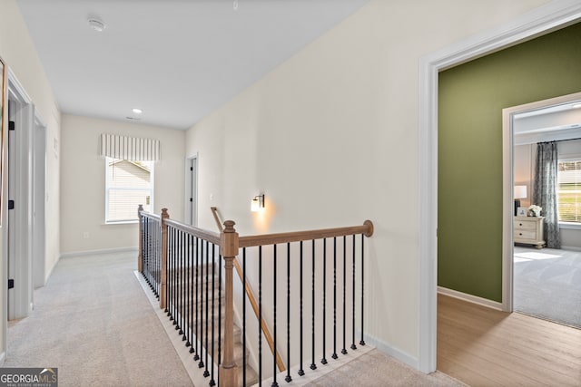 hall with a wealth of natural light, baseboards, light carpet, and an upstairs landing