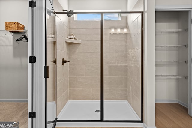 full bathroom featuring wood finished floors, a stall shower, a walk in closet, and baseboards