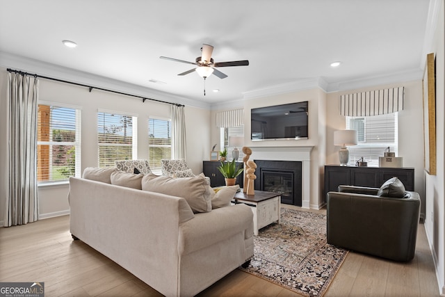 living area featuring ornamental molding, a glass covered fireplace, visible vents, and light wood-style floors