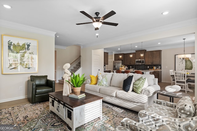 living room with dark wood-style floors, stairs, crown molding, baseboards, and ceiling fan with notable chandelier