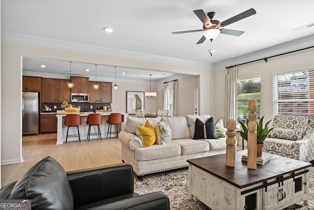 living area with light wood-style floors, visible vents, ornamental molding, and a ceiling fan