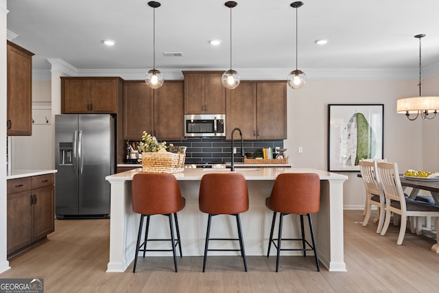 kitchen featuring stainless steel appliances, light countertops, a center island with sink, and pendant lighting