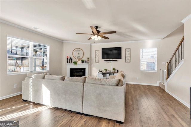 living area featuring hardwood / wood-style flooring, visible vents, stairway, a glass covered fireplace, and crown molding