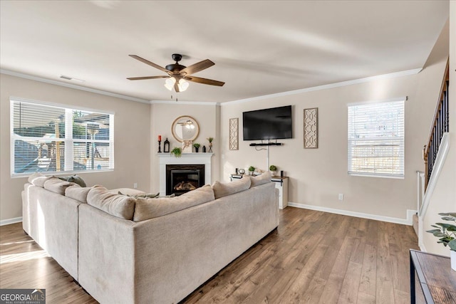 living area with crown molding, a glass covered fireplace, ceiling fan, wood finished floors, and baseboards