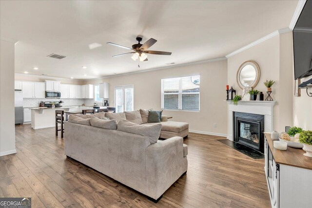 living room with dark wood-style floors, a fireplace, visible vents, and crown molding