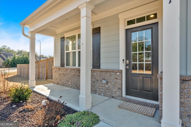 entrance to property featuring brick siding, a porch, and fence