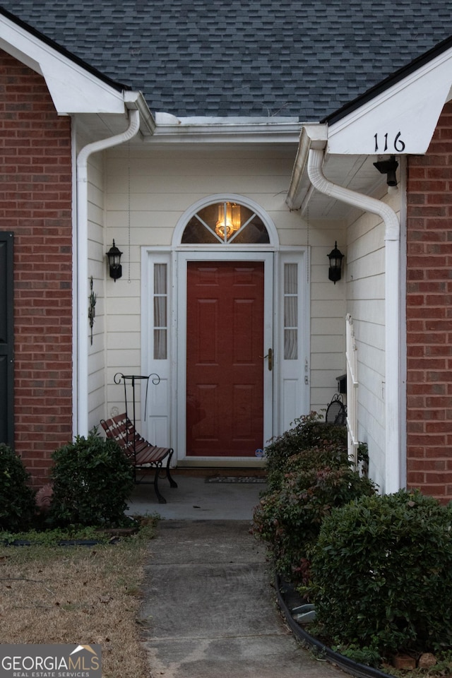 property entrance featuring a shingled roof and brick siding