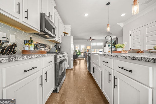 kitchen featuring crown molding, appliances with stainless steel finishes, white cabinetry, and light stone countertops