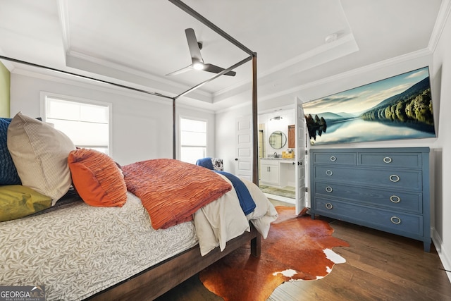 bedroom with dark wood-style floors, a tray ceiling, crown molding, and ensuite bathroom