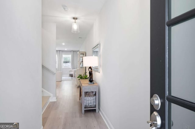 corridor featuring stairway, light wood-style flooring, and baseboards