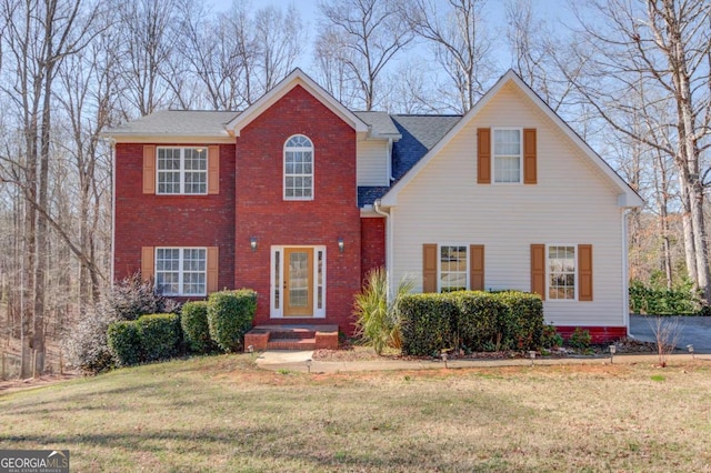 view of front facade featuring a shingled roof, a front yard, and brick siding