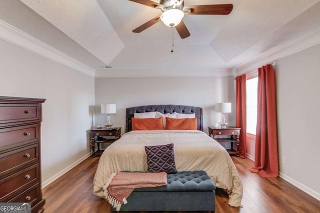 bedroom with ornamental molding, a tray ceiling, dark wood-style flooring, and baseboards