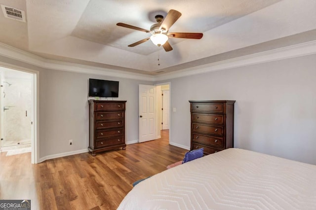 bedroom with light wood-style floors, a raised ceiling, visible vents, and baseboards